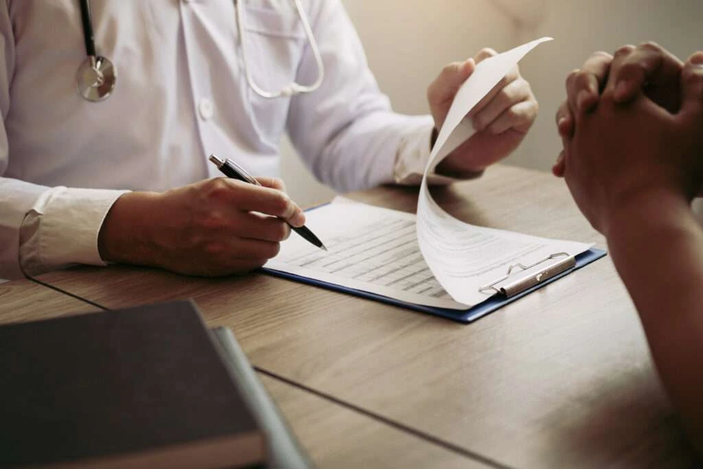 Doctor hand holding pen writing patient history list on note pad and talking to the patient about medication and treatment.