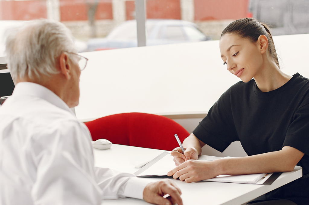 A young woman discusses paperwork with an older man at a desk, illustrating a compassionate and professional patient billing interaction in a healthcare setting.