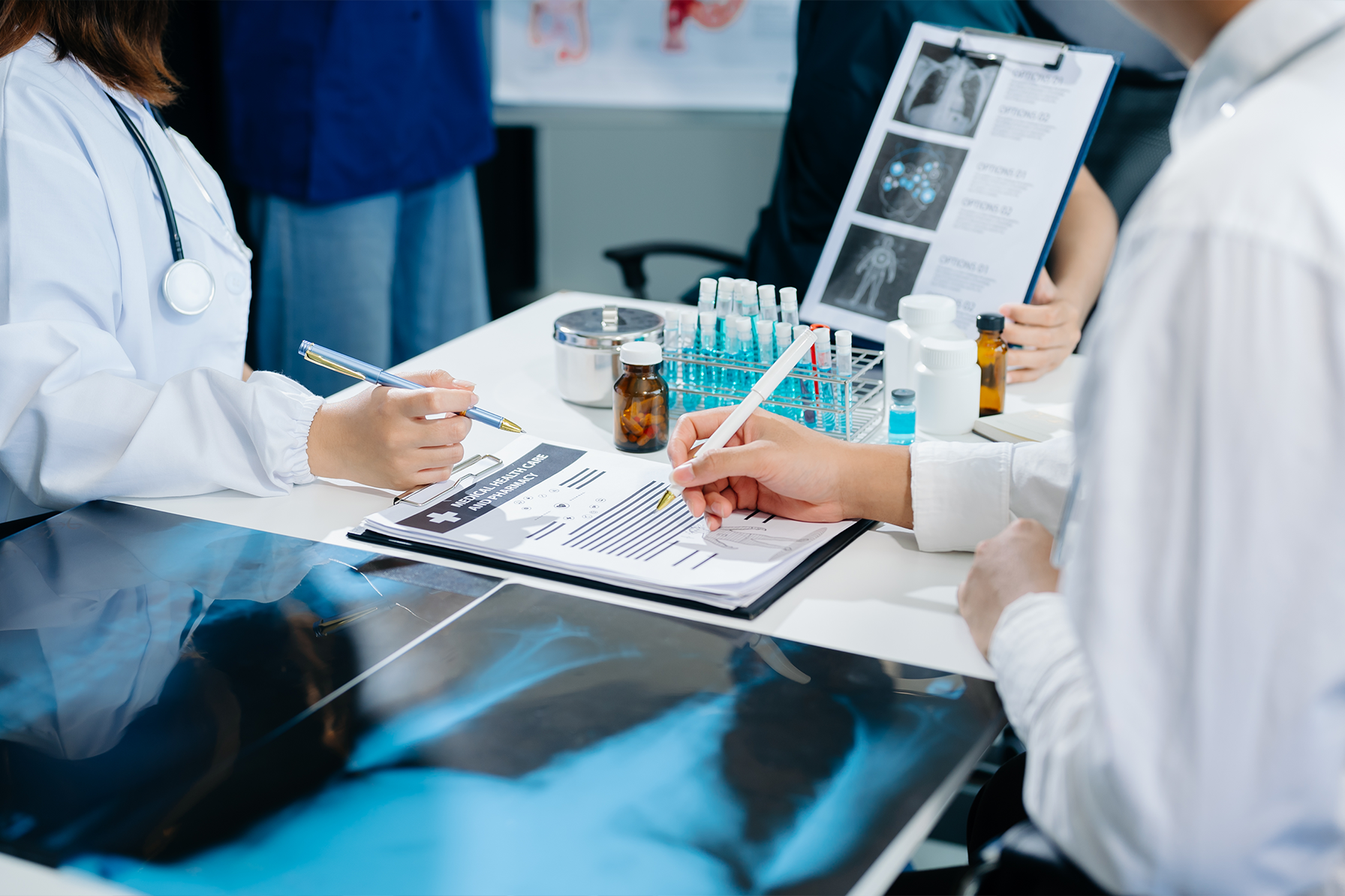 Healthcare professionals reviewing medical records, test tubes, and X-rays at a medical desk, illustrating the complexity of medical documentation and claims processing.